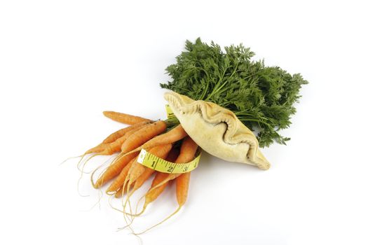 Contradiction between healthy food and junk food using bunch of carrots and pasty with a tape measure on a reflective white background 