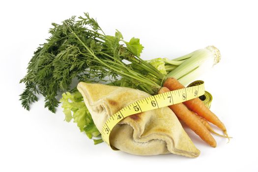 Contradiction between healthy food and junk food using a bunch of carrots and pasty with a tape measure on a reflective white background 