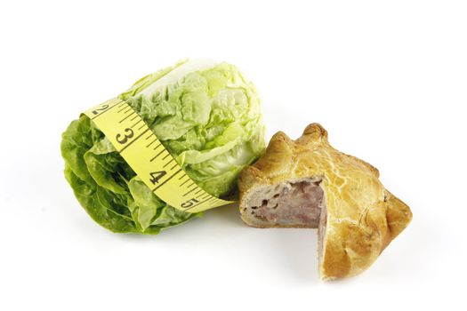 Contradiction between healthy food and junk food using a green salad lettace and pork pie with a yellow tape measure on a reflective white background 