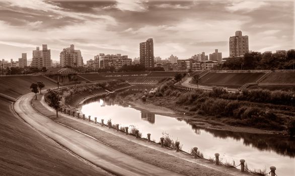Apartments and park near river in the modern city sunset evening.