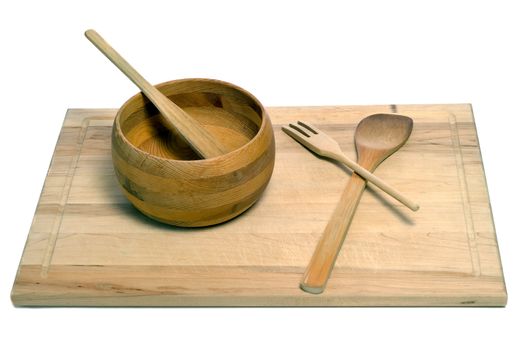 A set of wooden utensils including a spatula, fork, spoon, and bowl, all sitting on a wooden cutting board, isolated against a white background