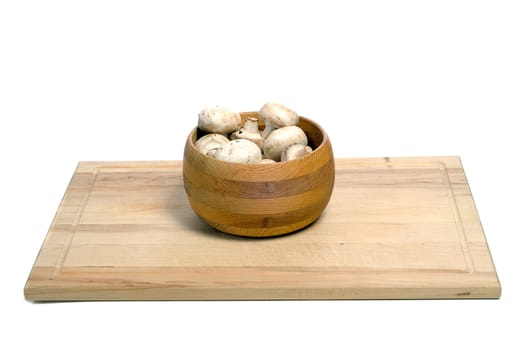 A wooden bowl of aged mushrooms shot on a wood cutting board, isolated against a white background