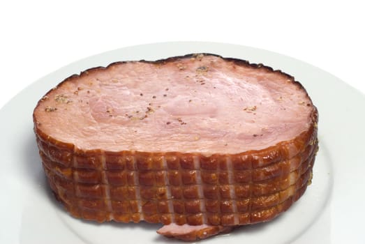 A cooked ham on a white plate, with spices on top, isolated against a white background