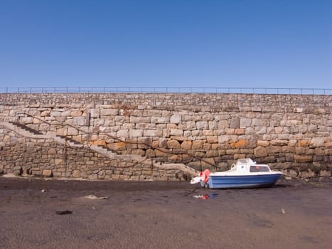 Boat on sand, steps lead down from Trefor harbour wall. Wales UK.