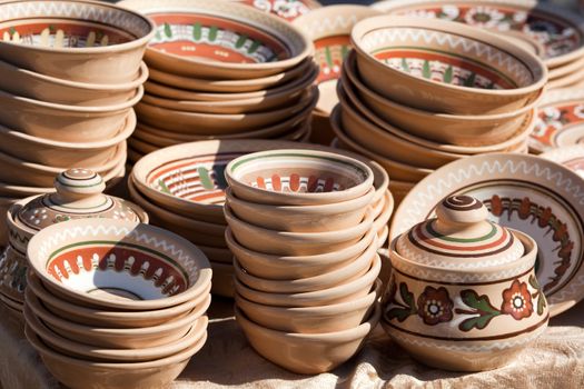 Stack of rustic handmade ceramic brown plates and pots decorated by traditional ornament and pattern at the handicraft market