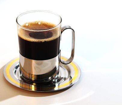 A glass of hot coffee on a saucer.