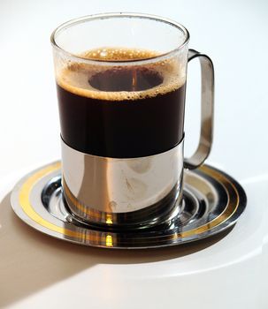 A glass of hot coffee on a saucer.