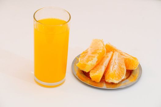 Orange juice in a glass and orange wedges on the saucer.
