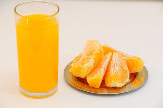 Orange juice in a glass and orange wedges on the saucer.