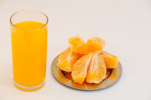 Orange juice in a glass and orange wedges on the saucer.