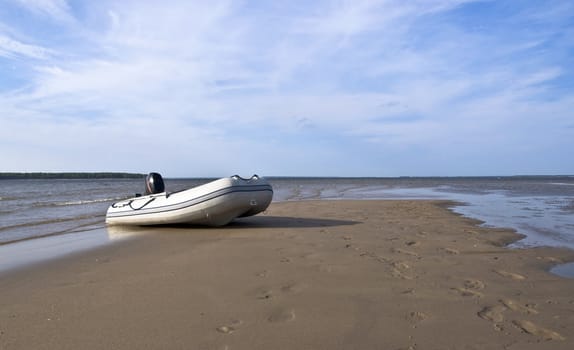 Inflatable fishing boat with an engine standing on a deserted beach on the background of blue sky with clouds. Landscape. 