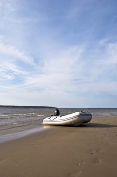 Inflatable fishing boat with an engine standing on a deserted beach on the background of blue sky with clouds. Landscape. 