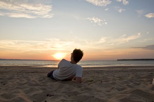 Young man lying on the beach back to the camera and watching the sunset. Summer Landscape.