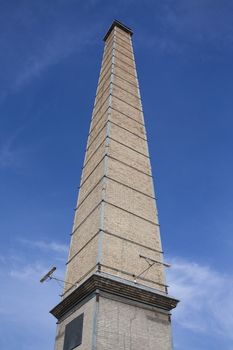 Nineteenth century brick gasworks chimney against blue sky and white clouds.