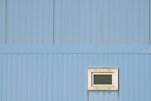 Very small window in blue industrial facade. Focus on lower half, which is the foreground. Geometrical abstract.