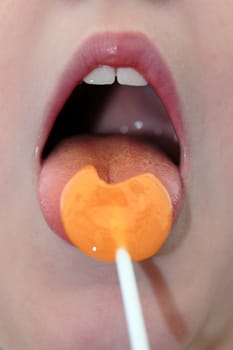 young girl licking an orange lollipop into a heart shape