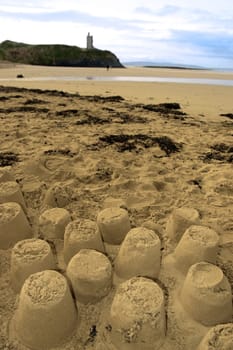 childrens sandcastles on a beach in ireland with cliffs and real castle in background