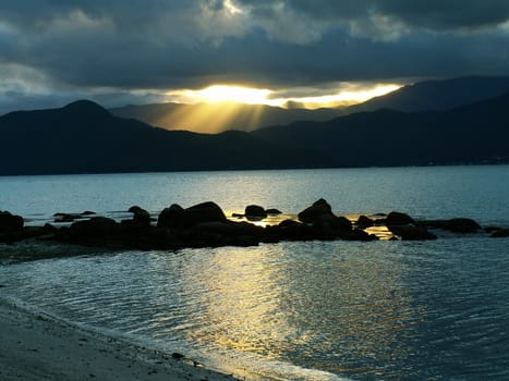 Yellow sun rays through clouds, passing over the mountains and making a nice reflection on the sea surface