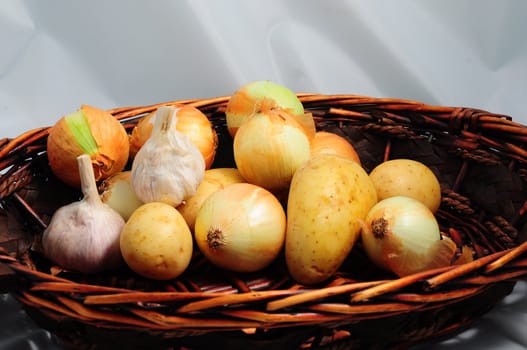 Potatoes  , garlic and onions on the wicker basket on the white backgrounds .