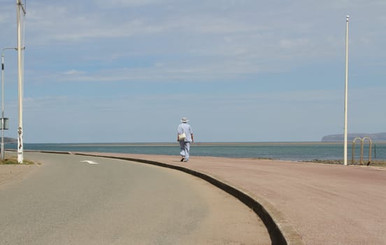 Senior woman in open space walking on pavement next to the sea.
