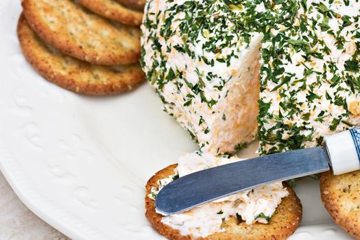 Herb cheese being spread onto a sesame cracker. 