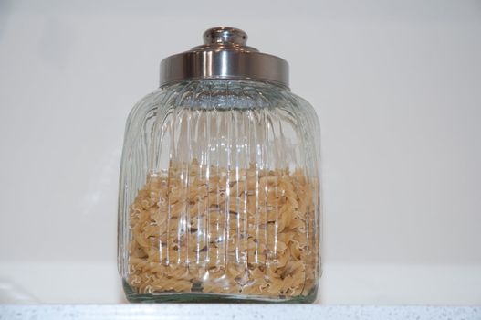 A glass jar with chrome lid. Inside the banks are located pasta.