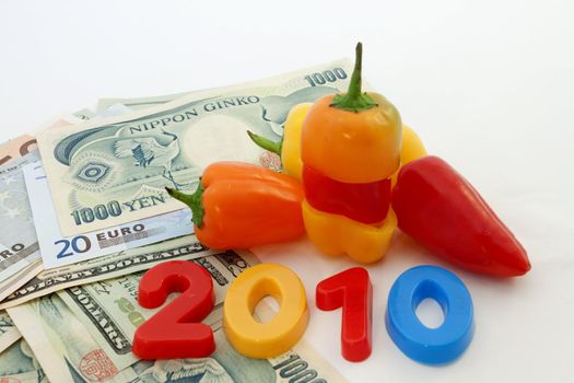 Odd cut and odd puzzle fit of colorful peppers paired with bright 2010 letters and world currencies suggest the global connectiveness of 21st century economies.