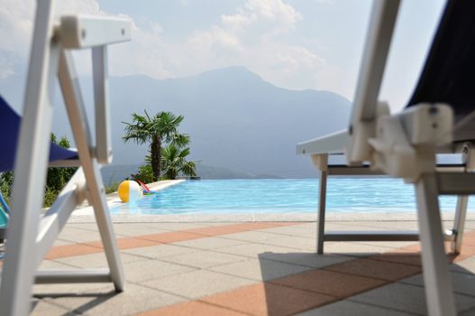 View over great swimming pool with palms, toys and chairs, mountains in the background