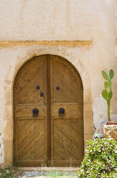 Wooden old style door with wrought handles. Entrance in ancient Mediterranean stone house and cactus