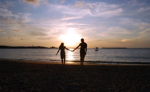 A couple is walking on the beach at the sunset. The ocean at the background and the sky with beautiful colors.