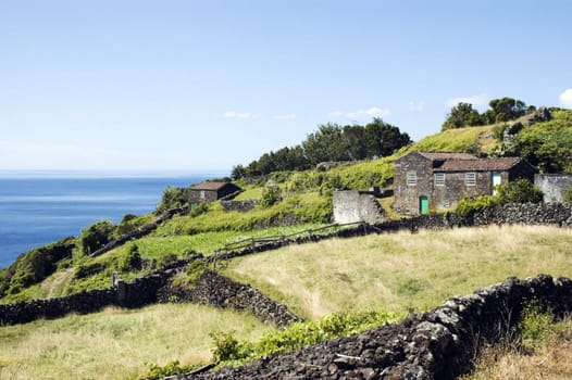 A hilly landscape with a small house next to an ocean. Taken in Azores, Portugal.