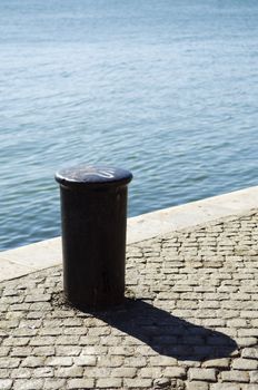 A view of a short, cylindrical metal post permanently attached to a pier or quay, often called a bollard to which a ship is tied while docked.