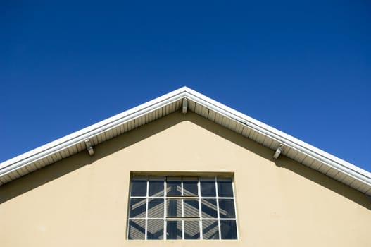 Part of a wooden roof with window as detail of a warehouse in front of blue sky background