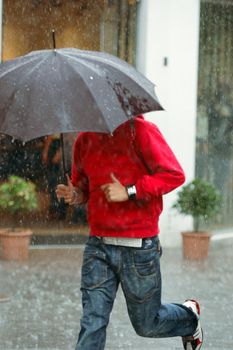 A man is running in the rain with an unbrella. Motion blur because of the running and the rain. 