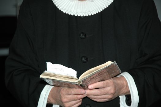 A priest is reading from a bible. The bible seams very old.