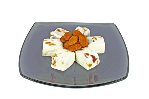 Delicious nougat with almonds on black glass plate, isolated on white