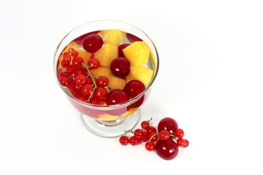 Peach compote with fresh red currants and sour cherries in glass isolated on white