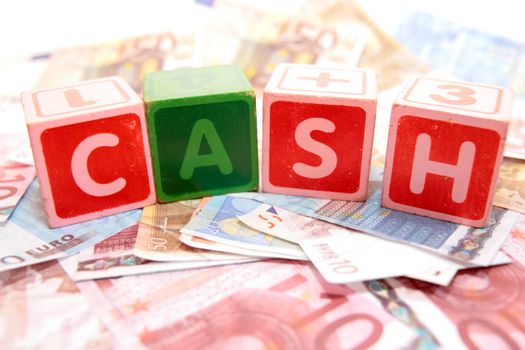 assorted childrens toy letter building blocks against a white background on money that spell cash