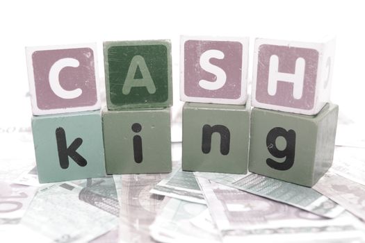 assorted childrens toy letter building blocks against a white background on money that spell cash king