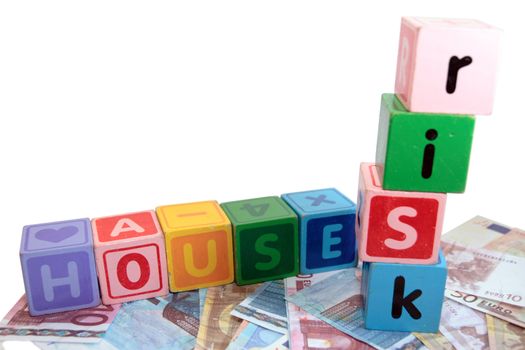 assorted childrens toy letter building blocks against a white background on money that spell house risk