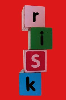 assorted childrens toy letter building blocks against a red background that spell risk