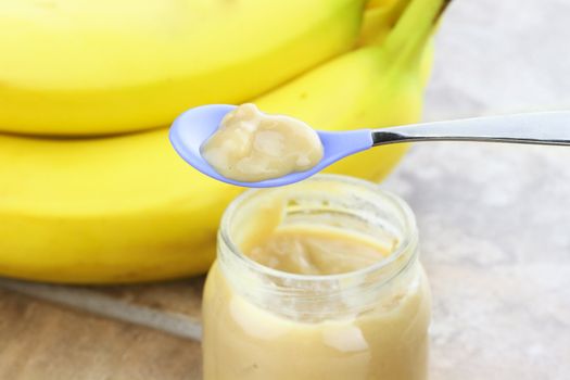 Pureed baby food from a jar with fresh bananas in background.