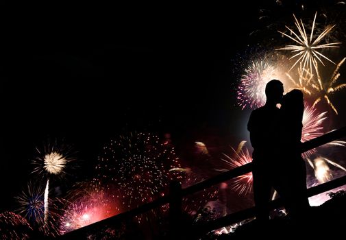 A silhouette of a kissing couple in front of a huge fireworks display.