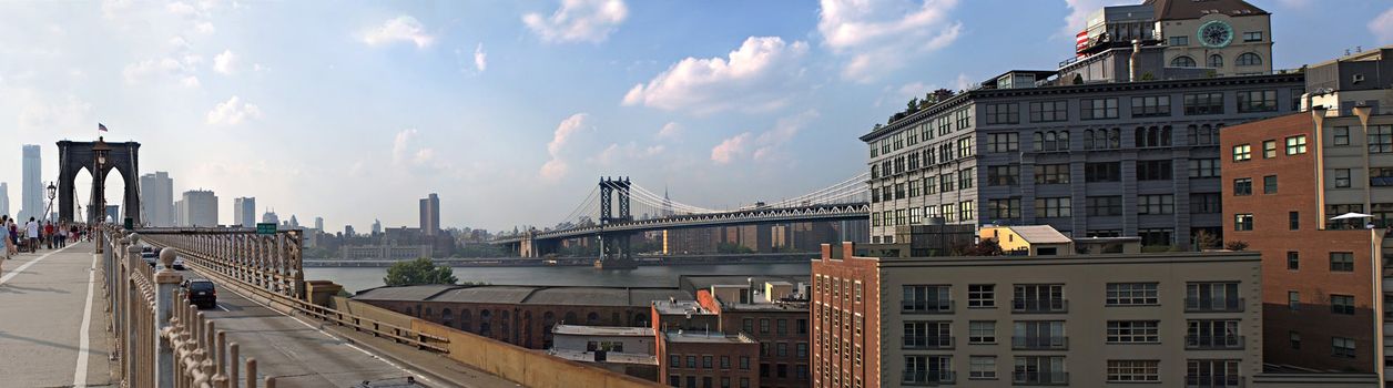 A panoramic image of the New York City skyline including the Brooklyn bridge the Manhattan bridge with the Empire State building in the far distance.