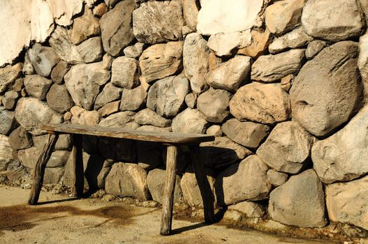 old wood bench up against a rock wall
