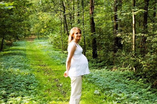 Young woman in pregnancy on walk in park in midday (southern) Poland .