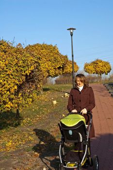 Young mother is walking in park with baby carriage
