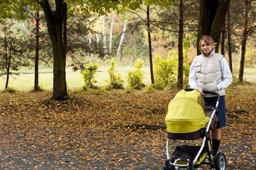 Young mother is walking in park with baby carriage