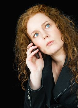 Beautiful girl with red hair speaking in mobile phone, seen against black background