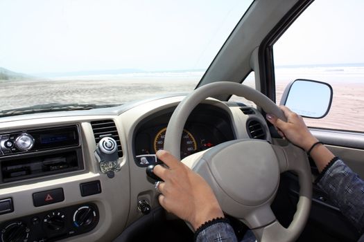 A view of the dashboard and steering of a car being driven on a beach.